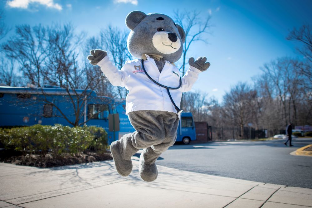 Children's National Hospital mascot Dr. Bear jumps in the air against a bright blue sky background