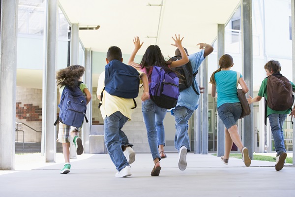 Kids wearing backpacks run down a school hallway.