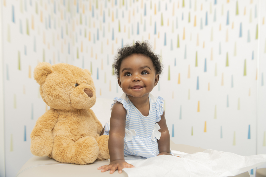 Smiling baby seated next to a large teddy bear
