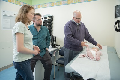 Dr. Marc Levitt holds the hand of a baby on an exam table.