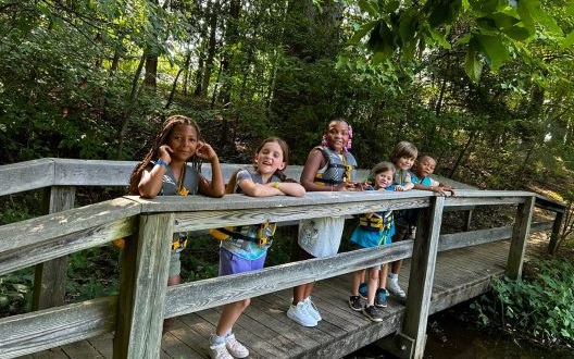 A group of girls smile while standing on a wooden bridge at Camp New Friends.