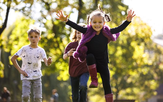 Two girls and a boy run outside on a sunny day