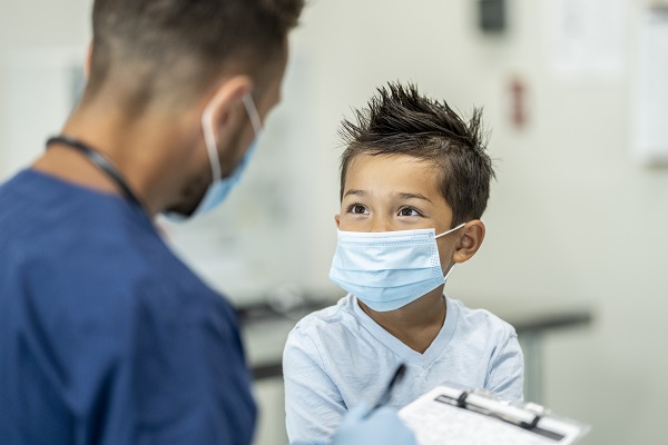 A boy and a nurse, both wearing masks, look at each other during an appointment.